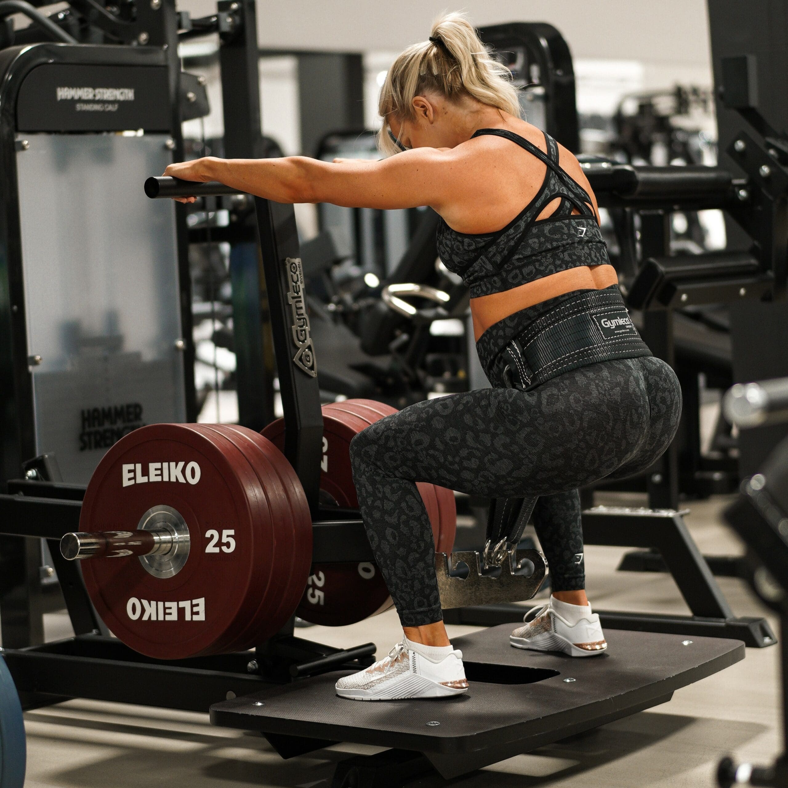 Vrouw voert een belt squat uit op een machine met gewichtsschijven, met focus op benen en minimale belasting van de onderrug